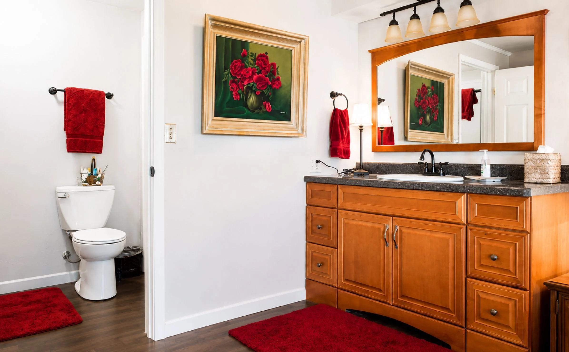 Bathroom with warm wood dual vanity, dark granite countertops, red towels, and pendant lights in a Scurlock Farms rental in