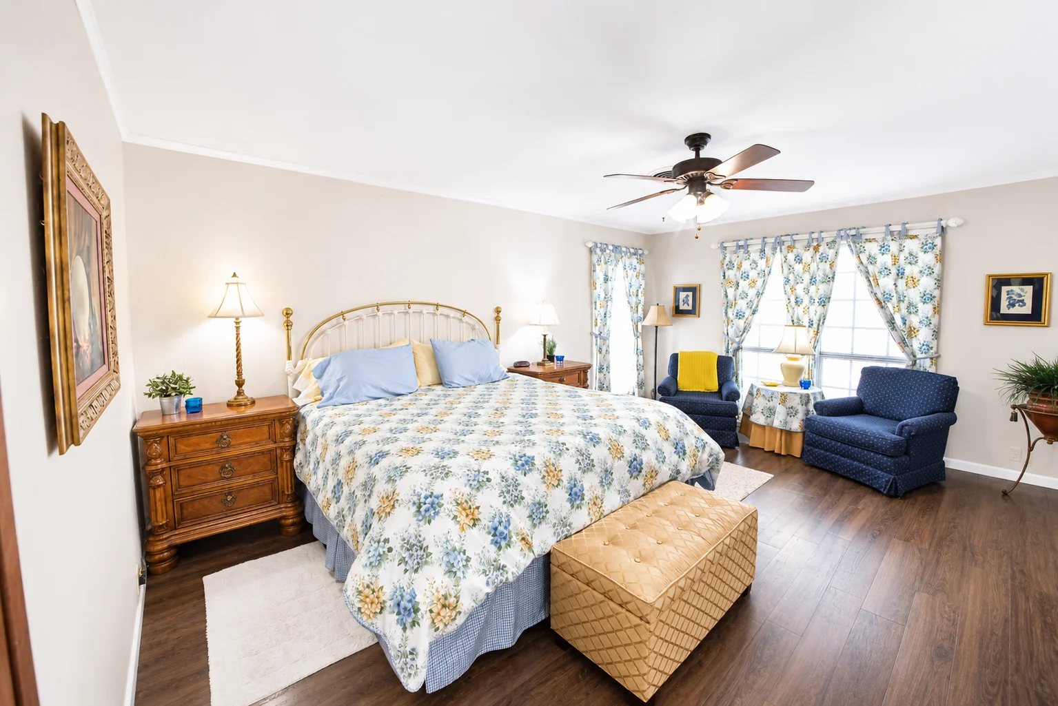 Master bedroom with brass bed frame, floral bedding, and navy chairs by large windows at a Scurlock Farms cabin in