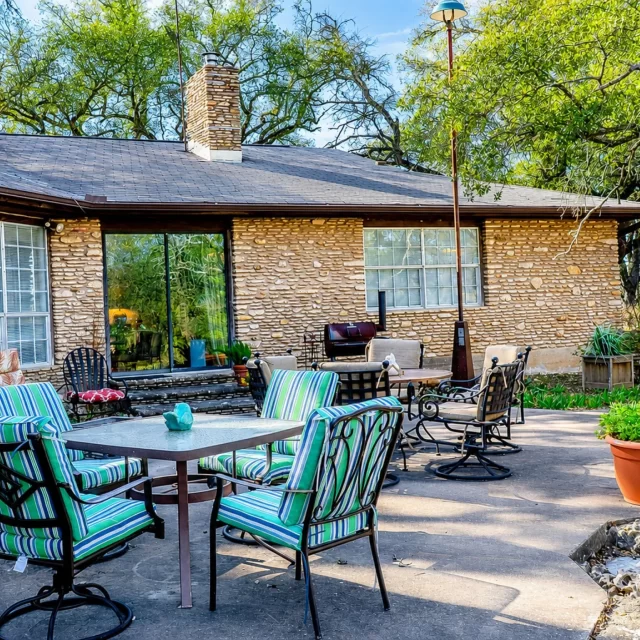 Family reunion cabin patio with striped lounge chairs and stone dining table beside a rustic stone cottage in Georgetown, TX
